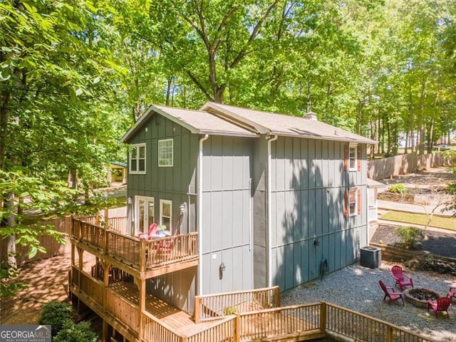 rear view of house with fence, a wooden deck, a fire pit, and a chimney