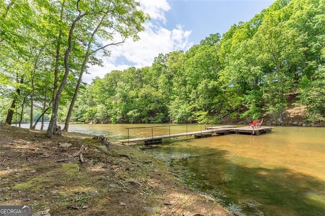 view of yard with a water view, a floating dock, and a forest view