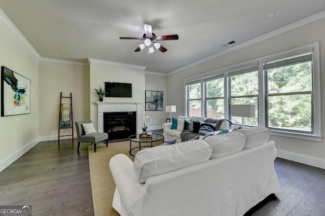 living room featuring a ceiling fan, baseboards, dark wood finished floors, a glass covered fireplace, and ornamental molding