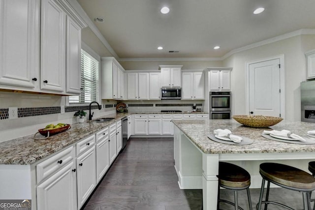 kitchen featuring appliances with stainless steel finishes, a sink, white cabinets, a breakfast bar area, and recessed lighting