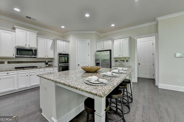 kitchen featuring stainless steel appliances, white cabinets, a center island, dark wood-type flooring, and a breakfast bar area