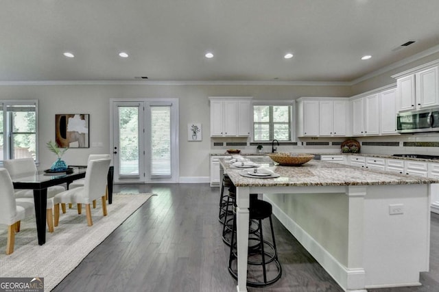 kitchen featuring stainless steel microwave, a kitchen island, white cabinetry, light stone countertops, and recessed lighting