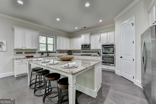 kitchen with appliances with stainless steel finishes, a kitchen island, white cabinets, ornamental molding, and light stone counters
