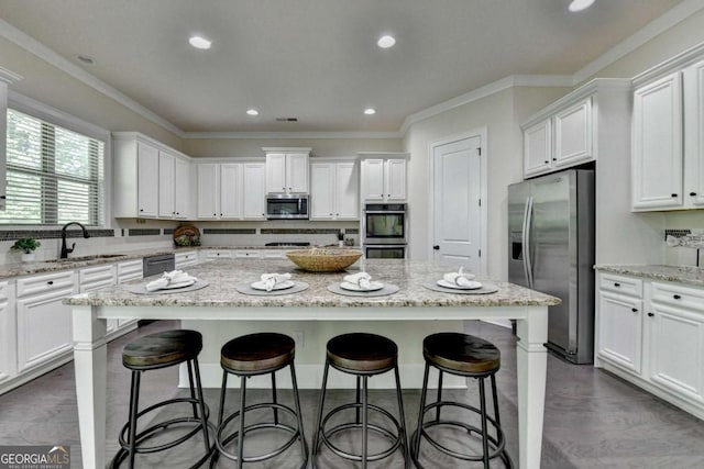 kitchen featuring stainless steel appliances, a sink, white cabinets, a center island, and ornamental molding