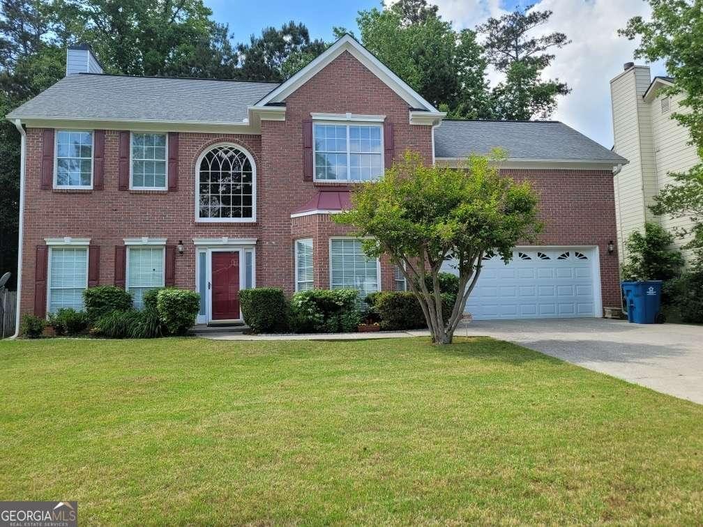 colonial inspired home with concrete driveway, brick siding, a front yard, a garage, and a chimney