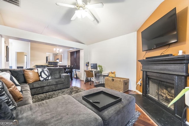 living area with vaulted ceiling, a fireplace with raised hearth, visible vents, and wood finished floors