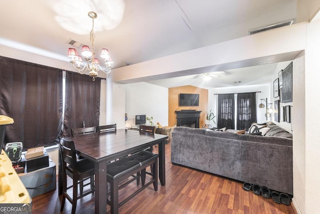 dining space with wood finished floors, visible vents, a fireplace, and ceiling fan with notable chandelier
