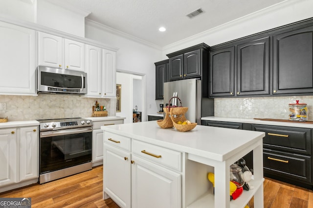 kitchen with appliances with stainless steel finishes, ornamental molding, white cabinets, light countertops, and backsplash