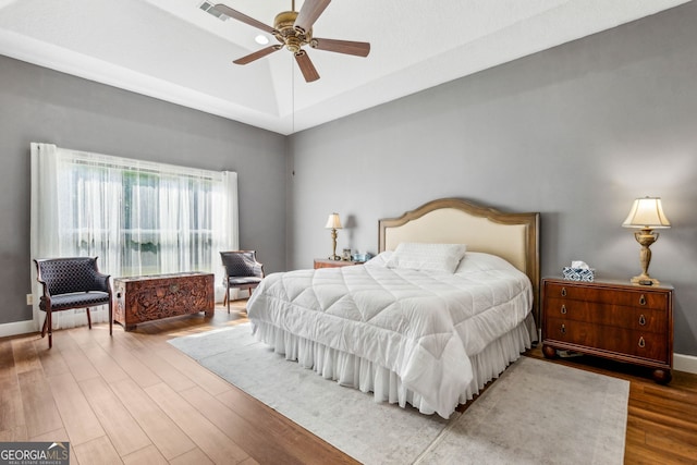 bedroom with wood finished floors, a raised ceiling, a ceiling fan, and baseboards