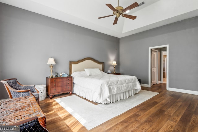 bedroom featuring wood finished floors, baseboards, a raised ceiling, and ceiling fan