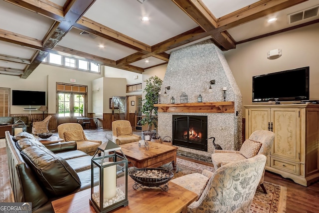 living area with coffered ceiling, beam ceiling, a large fireplace, and wood finished floors