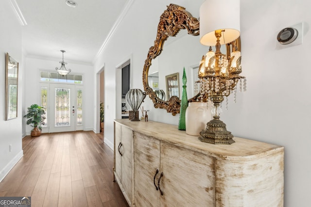hall featuring crown molding, wood finished floors, baseboards, and a chandelier