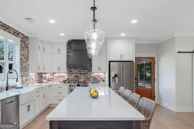 kitchen with a sink, stainless steel appliances, a wealth of natural light, light countertops, and custom range hood