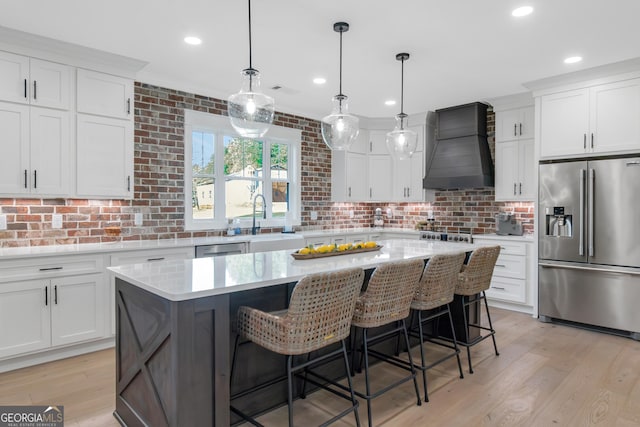 kitchen with light wood finished floors, appliances with stainless steel finishes, a kitchen island, and custom range hood