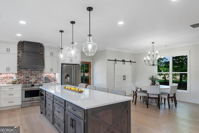 kitchen with custom exhaust hood, a barn door, white cabinets, and appliances with stainless steel finishes