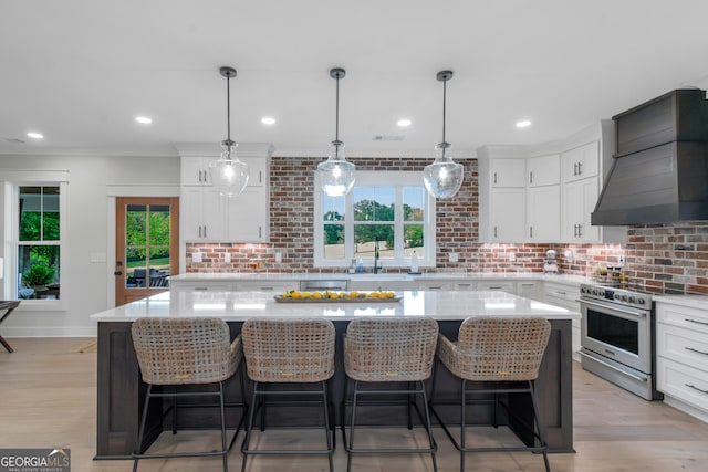 kitchen with a sink, stainless steel electric stove, white cabinetry, premium range hood, and light countertops