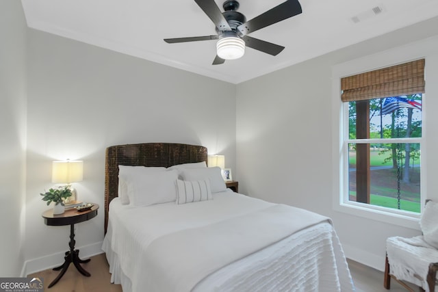 bedroom featuring wood finished floors, crown molding, visible vents, baseboards, and ceiling fan