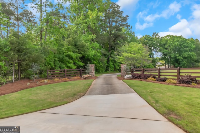 view of community featuring a yard, fence, and concrete driveway