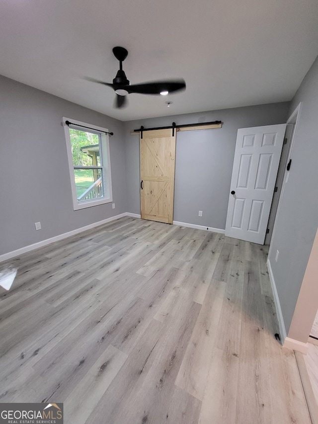 unfurnished bedroom with ceiling fan, a barn door, baseboards, and light wood-style floors