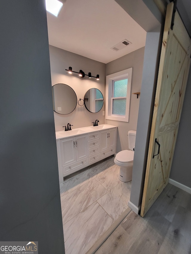 bathroom with toilet, visible vents, double vanity, and a sink