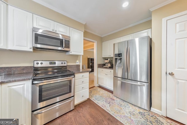 kitchen with appliances with stainless steel finishes, wood finished floors, white cabinetry, crown molding, and dark countertops
