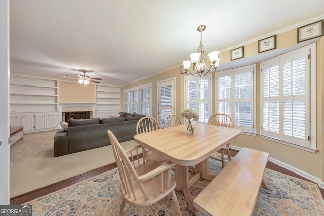 dining space with a chandelier, built in shelves, a ceiling fan, crown molding, and baseboards
