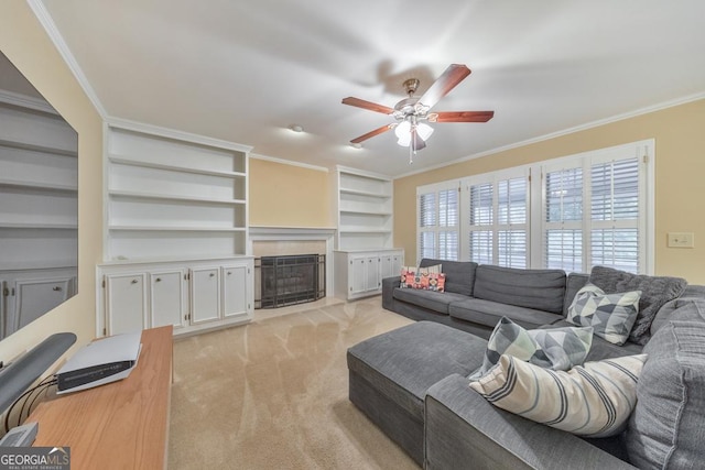 living room featuring crown molding, light carpet, ceiling fan, a fireplace, and built in shelves