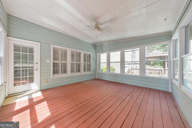 unfurnished sunroom with wood-type flooring, a ceiling fan, healthy amount of natural light, and wood walls
