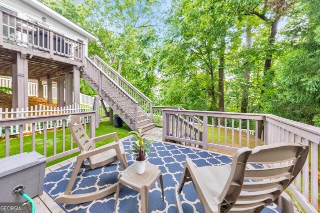 view of patio / terrace with a deck, stairway, view of wooded area, and fence