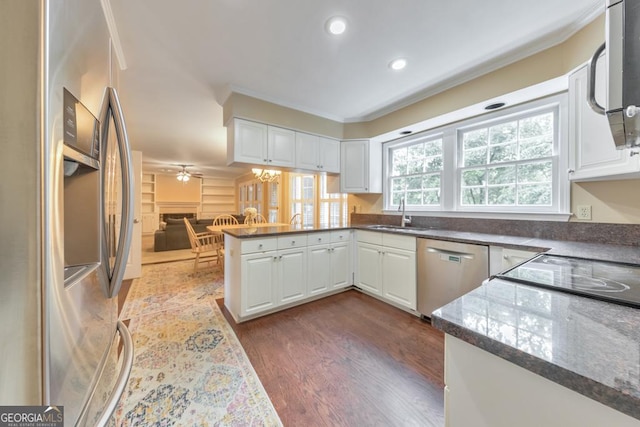 kitchen featuring appliances with stainless steel finishes, a peninsula, a sink, dark wood finished floors, and white cabinetry
