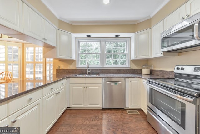 kitchen featuring appliances with stainless steel finishes, a sink, white cabinetry, ornamental molding, and dark stone countertops