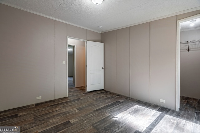 unfurnished bedroom with dark wood-style flooring, a decorative wall, crown molding, and a walk in closet