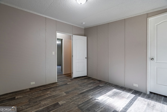 unfurnished bedroom featuring crown molding, a textured ceiling, a decorative wall, and dark wood finished floors