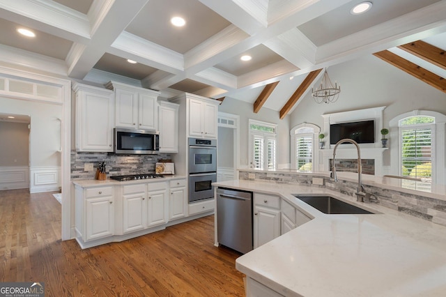 kitchen with a sink, appliances with stainless steel finishes, beamed ceiling, white cabinetry, and backsplash