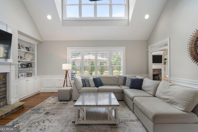 living area featuring a fireplace, high vaulted ceiling, built in shelves, wainscoting, and wood finished floors