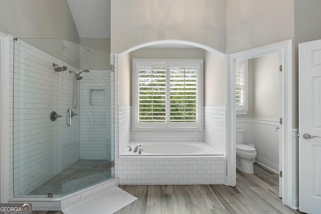bathroom featuring a stall shower, wood finished floors, toilet, a garden tub, and wainscoting