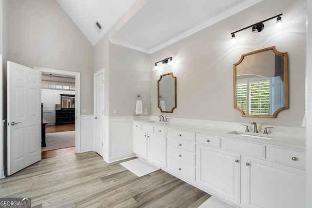 full bathroom with wood finished floors, vaulted ceiling, a wainscoted wall, double vanity, and crown molding