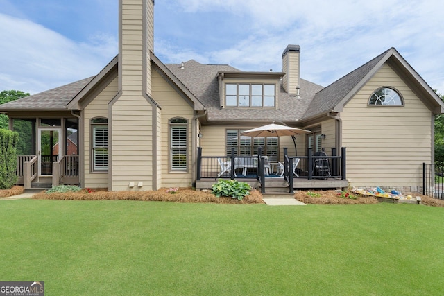rear view of property featuring a chimney, roof with shingles, a wooden deck, and a yard