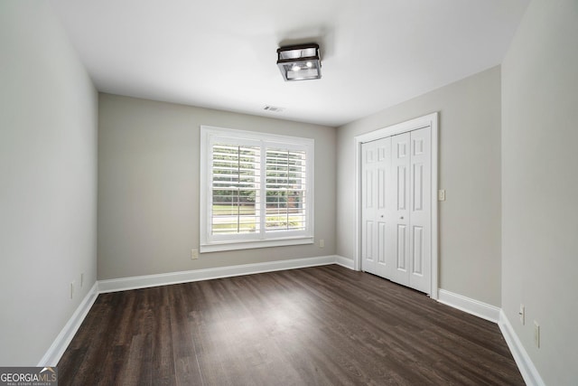 unfurnished bedroom with dark wood-style flooring, baseboards, and a closet