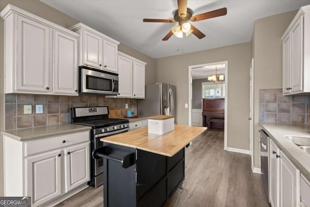 kitchen with ceiling fan with notable chandelier, light wood-style flooring, white cabinetry, backsplash, and appliances with stainless steel finishes