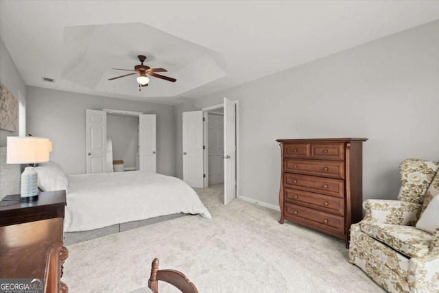 bedroom featuring a tray ceiling, visible vents, baseboards, ceiling fan, and light colored carpet