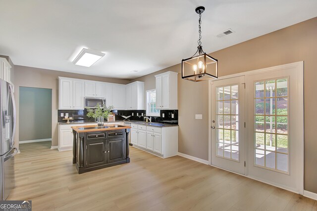kitchen with appliances with stainless steel finishes, white cabinetry, light wood-style floors, a chandelier, and healthy amount of natural light
