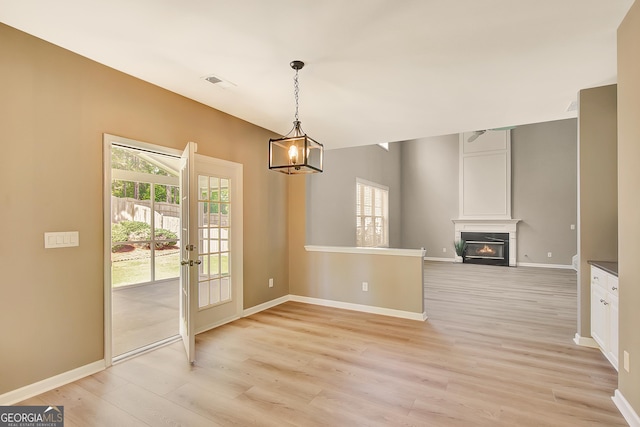 unfurnished dining area featuring light wood-style flooring, a warm lit fireplace, and baseboards