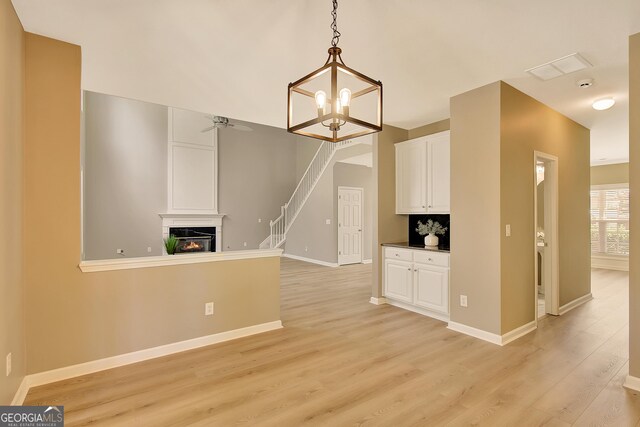 unfurnished dining area with light wood-style floors, a chandelier, stairway, a glass covered fireplace, and baseboards