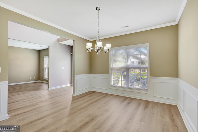 unfurnished dining area featuring a chandelier, light wood finished floors, plenty of natural light, wainscoting, and ornamental molding