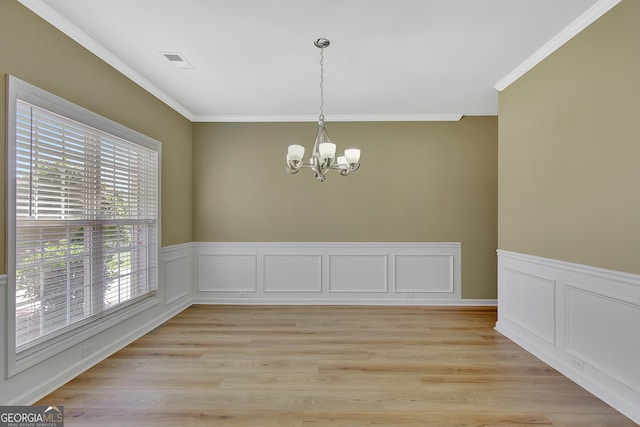 unfurnished dining area featuring a chandelier, crown molding, a wainscoted wall, light wood finished floors, and a decorative wall