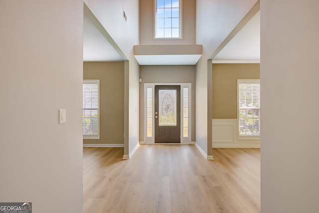 entrance foyer with light wood-style floors, a towering ceiling, and baseboards