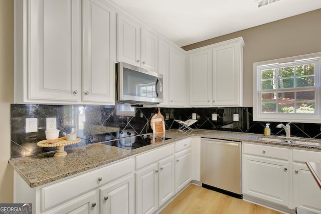 kitchen featuring stainless steel appliances, white cabinetry, a sink, light stone countertops, and decorative backsplash