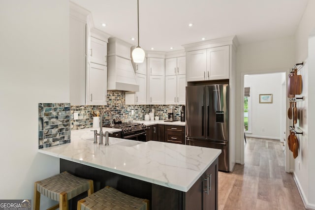 kitchen with light stone counters, built in fridge, a peninsula, premium range hood, and stainless steel range with gas cooktop