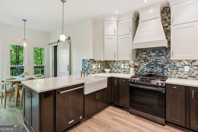 kitchen with custom exhaust hood, a sink, white cabinetry, light wood-style floors, and stainless steel appliances